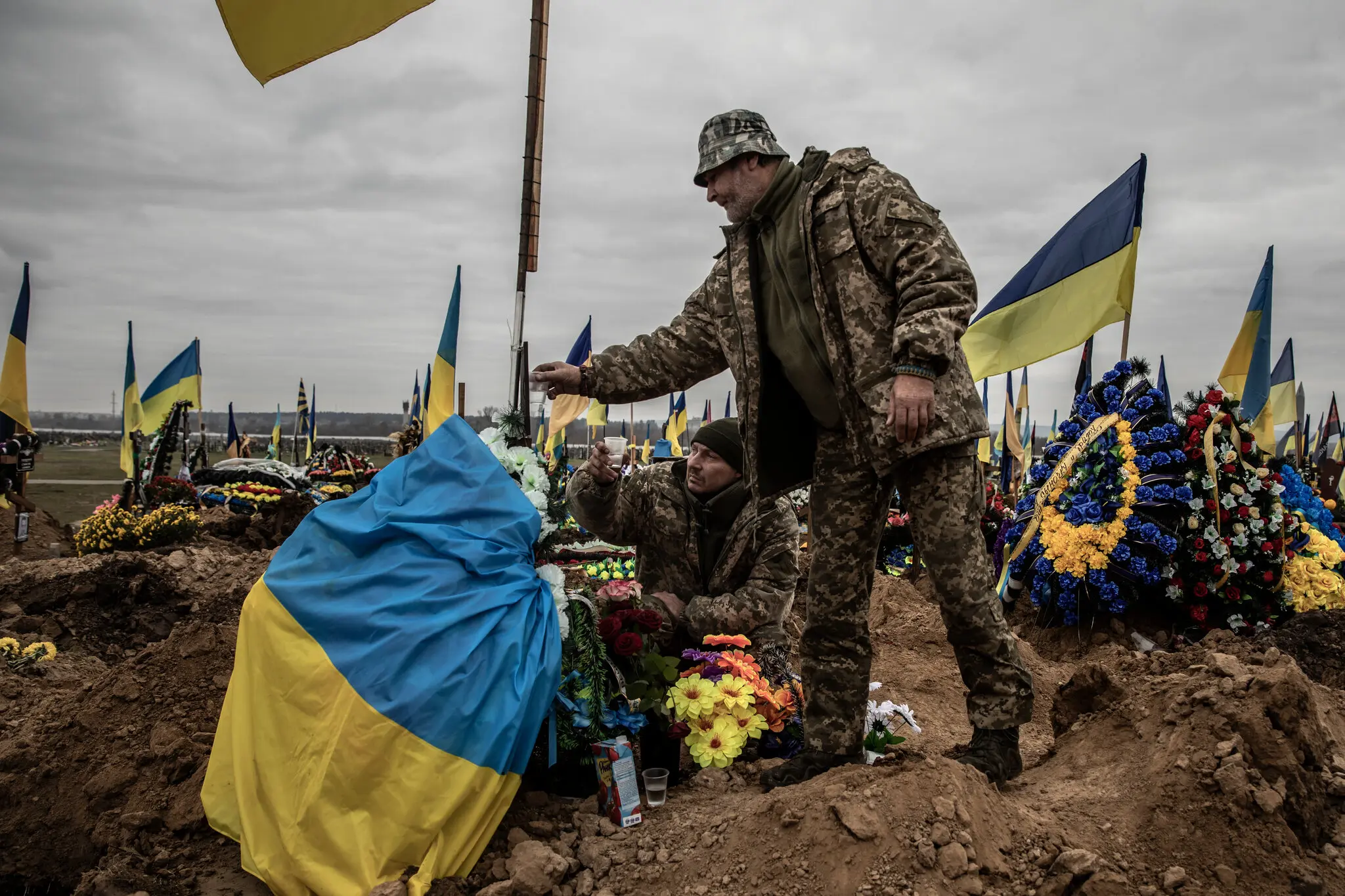 Серед лісу українських прапорів солдати горілкою вшановують загиблого товариша